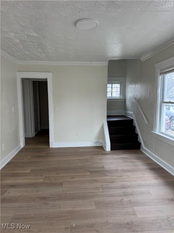 unfurnished room featuring stairway, wood finished floors, a textured ceiling, baseboards, and ornamental molding