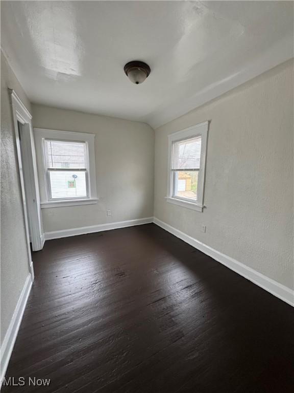 unfurnished room featuring dark wood finished floors, baseboards, and lofted ceiling