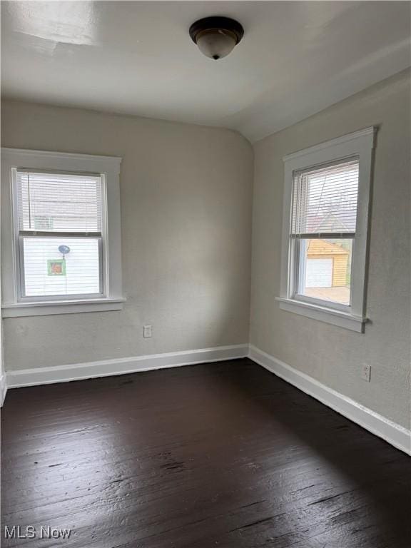 empty room with dark wood finished floors, baseboards, and a wealth of natural light