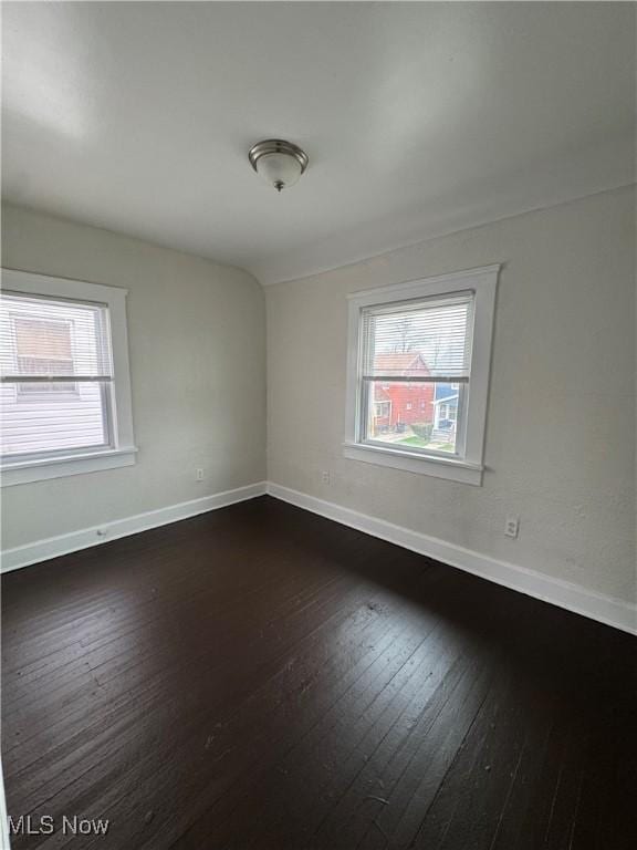 unfurnished room featuring baseboards, a wealth of natural light, and dark wood-style floors