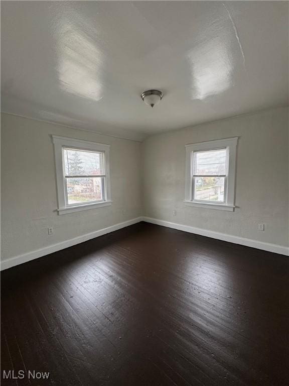 empty room with dark wood-type flooring, baseboards, and a wealth of natural light