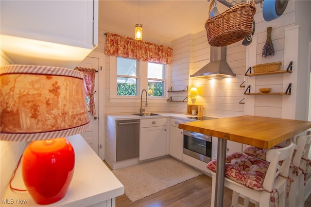 kitchen with a sink, stainless steel dishwasher, wall chimney range hood, white cabinets, and oven