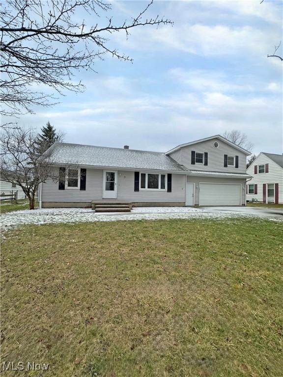 view of front of home with driveway, a front yard, an attached garage, and roof with shingles