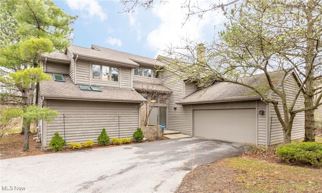 view of front of home with an attached garage, roof with shingles, driveway, and a chimney