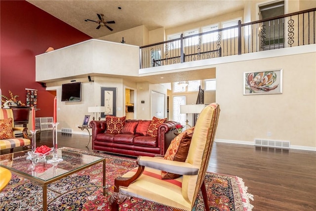 living room featuring visible vents, wood finished floors, baseboards, a high ceiling, and a ceiling fan