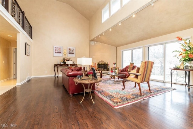 living room featuring baseboards, high vaulted ceiling, rail lighting, and wood finished floors