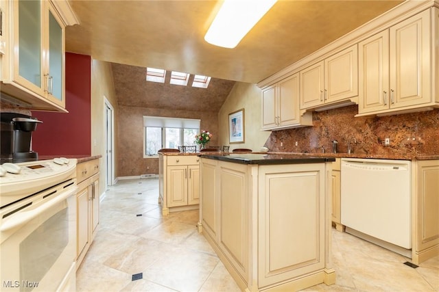 kitchen with decorative backsplash, dark countertops, white appliances, glass insert cabinets, and cream cabinetry