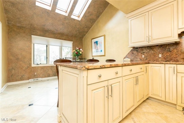 kitchen with a peninsula, light stone countertops, visible vents, and cream cabinetry