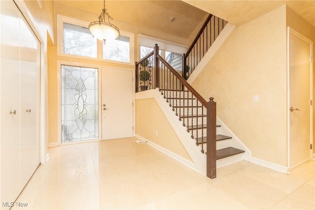 tiled foyer with stairway, baseboards, and a towering ceiling