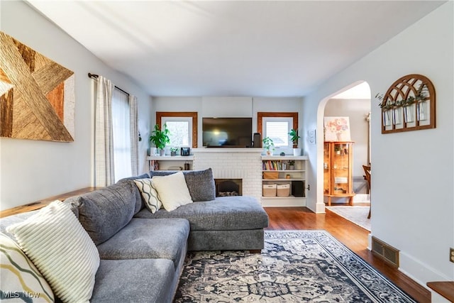 living room with a fireplace, baseboards, visible vents, arched walkways, and dark wood-type flooring