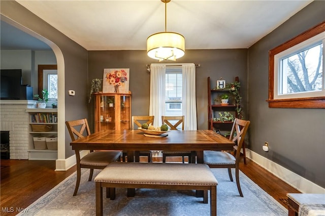 dining area featuring arched walkways, baseboards, and wood finished floors
