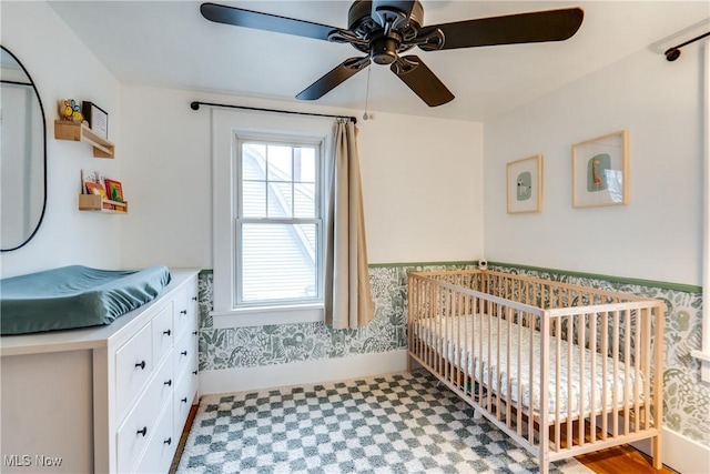 bedroom featuring baseboards, a wainscoted wall, a ceiling fan, and a nursery area