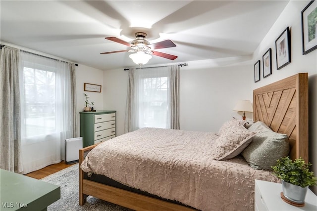 bedroom featuring a ceiling fan, multiple windows, and wood finished floors