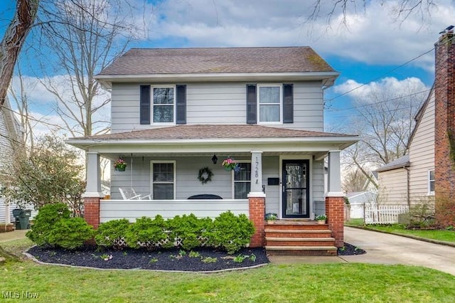 american foursquare style home with driveway, a shingled roof, a porch, and a front yard