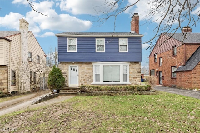 colonial home with a front lawn, a chimney, stone siding, and driveway