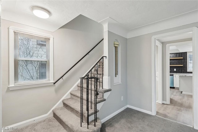 staircase featuring baseboards, carpet flooring, and a textured ceiling