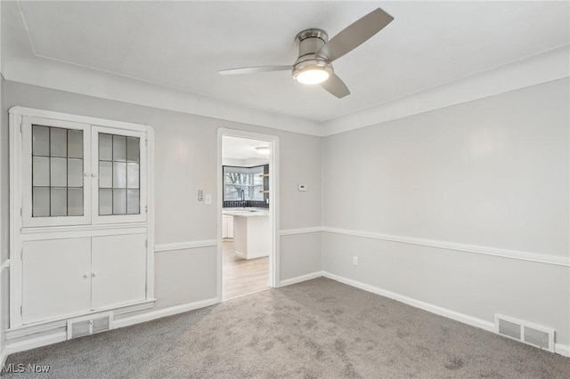 carpeted spare room with baseboards, visible vents, and a ceiling fan