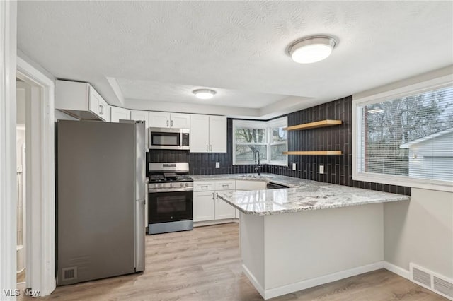 kitchen featuring a sink, backsplash, appliances with stainless steel finishes, a peninsula, and visible vents