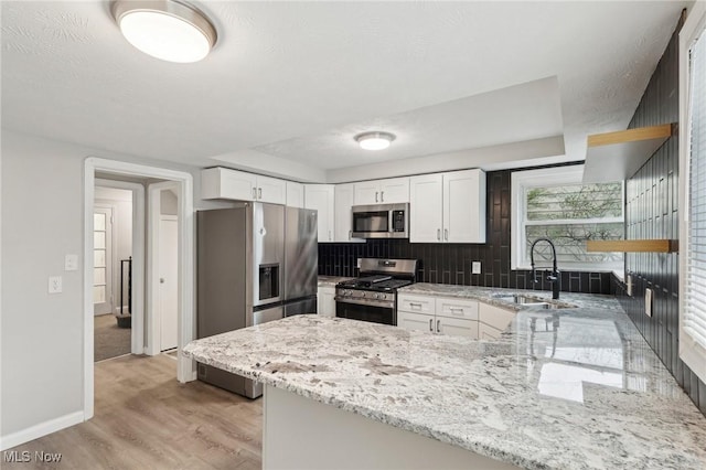 kitchen featuring stainless steel appliances, a sink, a peninsula, light wood-style floors, and light stone countertops