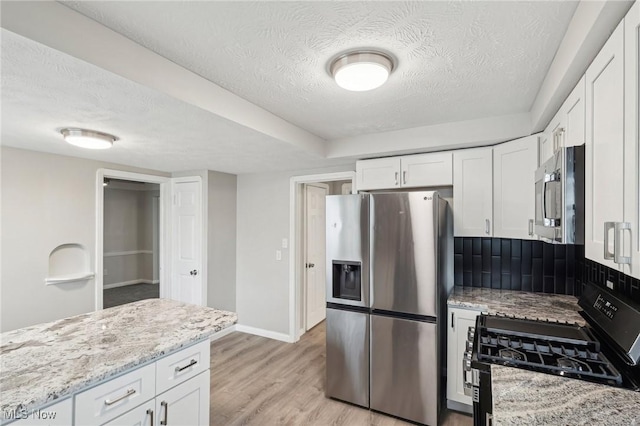 kitchen with white cabinetry, stainless steel appliances, backsplash, light stone counters, and light wood-style flooring