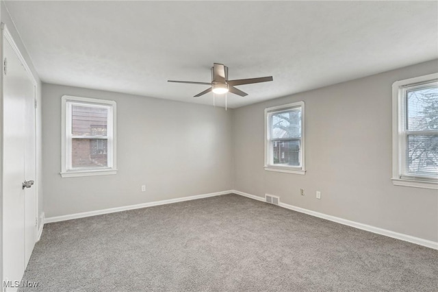 carpeted spare room featuring baseboards, visible vents, and ceiling fan