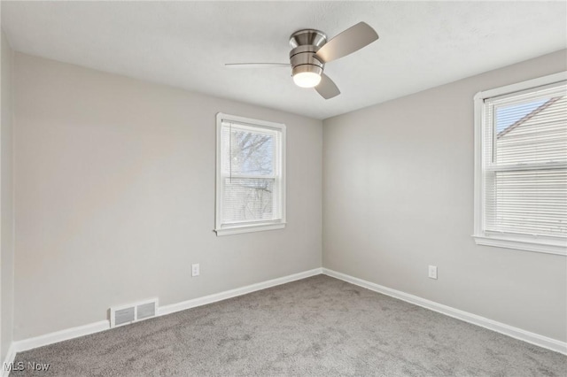 carpeted empty room featuring baseboards, a wealth of natural light, visible vents, and ceiling fan