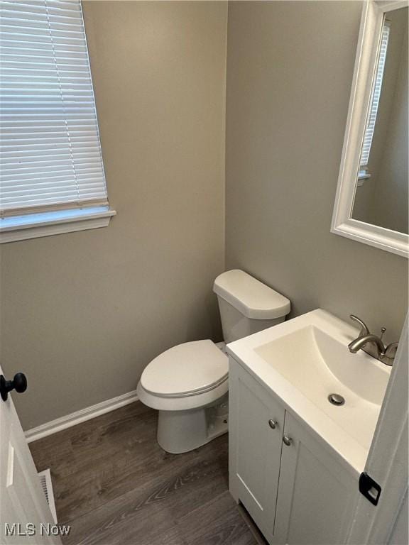 half bathroom with vanity, wood finished floors, a wealth of natural light, and toilet