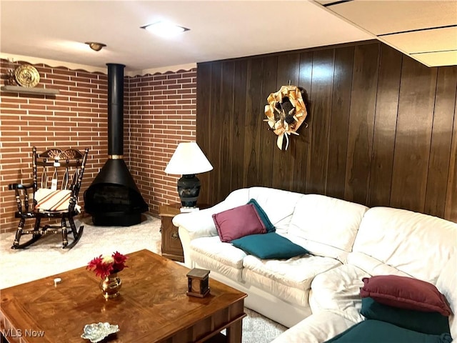 living area featuring carpet flooring, a wood stove, wooden walls, and brick wall
