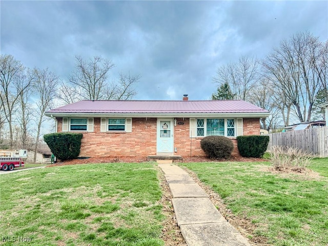 ranch-style home with metal roof, fence, a chimney, brick siding, and a front lawn
