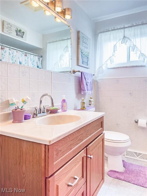bathroom with tile patterned floors, toilet, vanity, visible vents, and tile walls