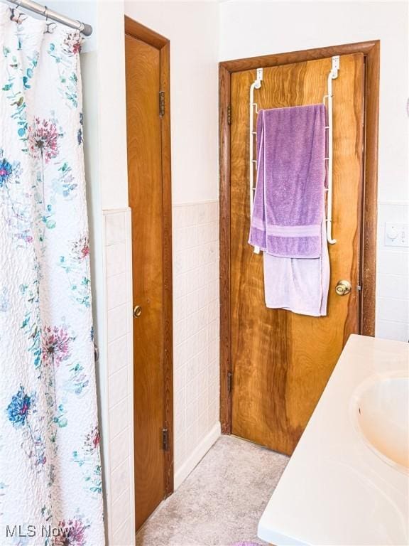 full bath featuring a wainscoted wall, a sink, a shower with shower curtain, and tile walls