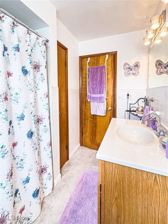full bathroom featuring tile walls, a shower with curtain, vanity, and wainscoting