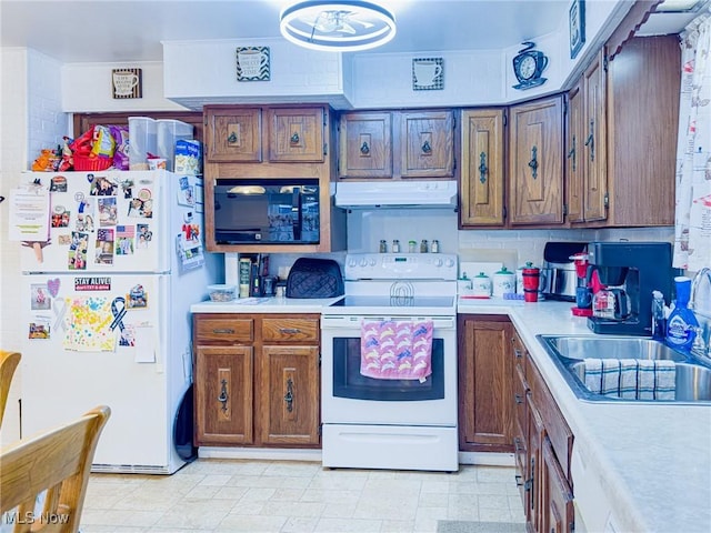 kitchen featuring light countertops, white appliances, under cabinet range hood, a sink, and brown cabinetry