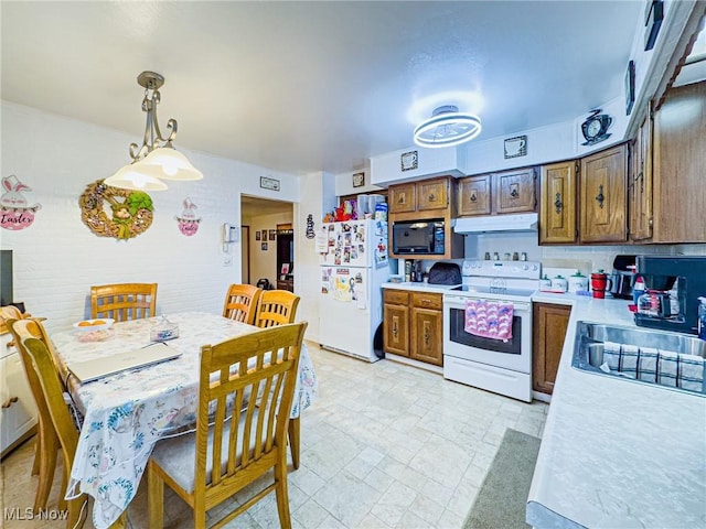 kitchen featuring light countertops, a sink, hanging light fixtures, under cabinet range hood, and white appliances