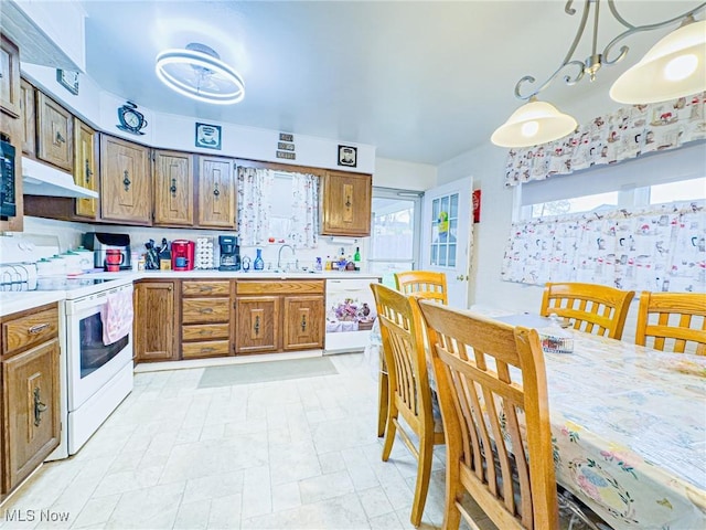 kitchen with light countertops, white appliances, under cabinet range hood, a sink, and brown cabinets