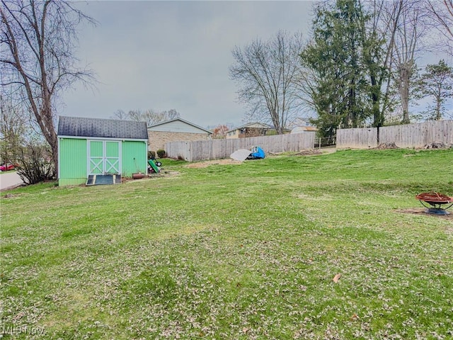 view of yard with an outdoor structure, a fenced backyard, an outdoor fire pit, and a storage shed