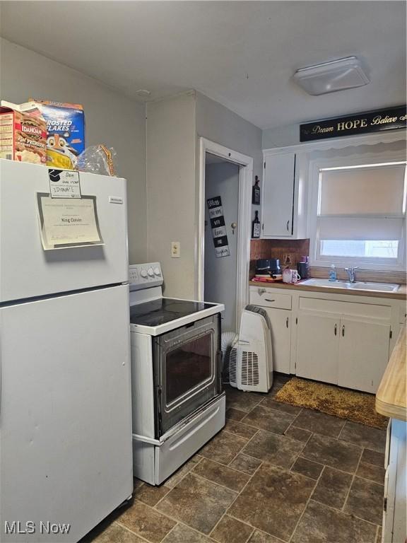 kitchen featuring white cabinets, stone finish flooring, a sink, freestanding refrigerator, and electric range