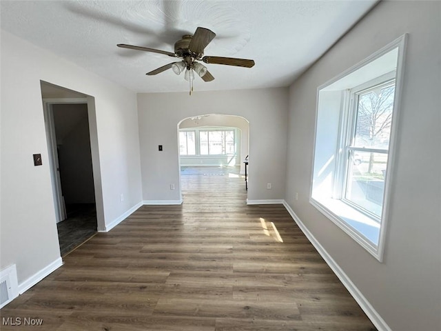 2106 17th St SW, Akron, OH 44314 - empty room featuring baseboards, arched walkways, ceiling fan, and dark wood-type flooring