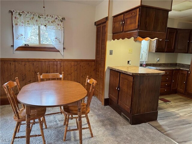 dining area with light wood-style flooring, wooden walls, and wainscoting