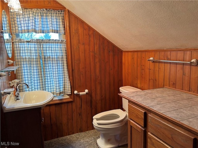 half bathroom with a textured ceiling, wood walls, toilet, vanity, and lofted ceiling