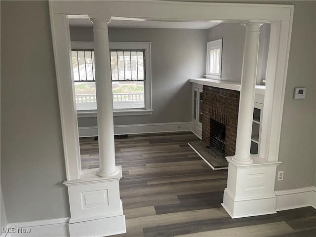 unfurnished living room featuring dark wood-type flooring, a fireplace, baseboards, and decorative columns
