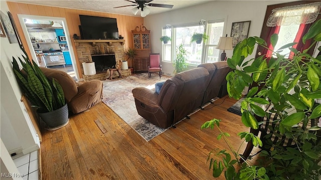 53525 Somerton Hwy, Jerusalem, OH 43747 - living room featuring a ceiling fan, hardwood / wood-style floors, a stone fireplace, and wooden walls