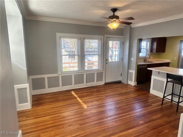 unfurnished dining area with a textured ceiling, crown molding, a ceiling fan, dark wood-type flooring, and a sink