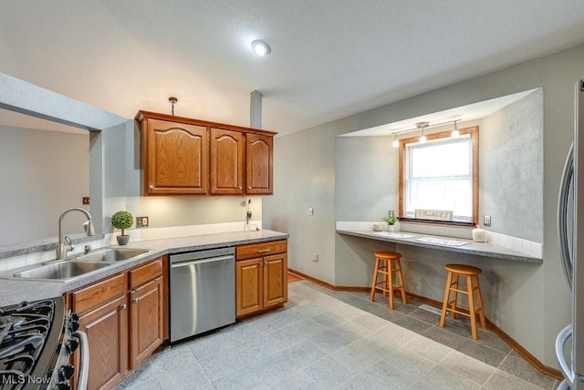 kitchen featuring a sink, a kitchen breakfast bar, appliances with stainless steel finishes, brown cabinetry, and baseboards