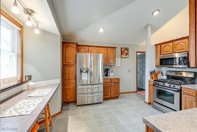 kitchen featuring light countertops, vaulted ceiling, brown cabinetry, and appliances with stainless steel finishes