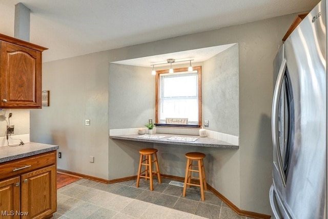 kitchen with freestanding refrigerator, baseboards, and brown cabinetry