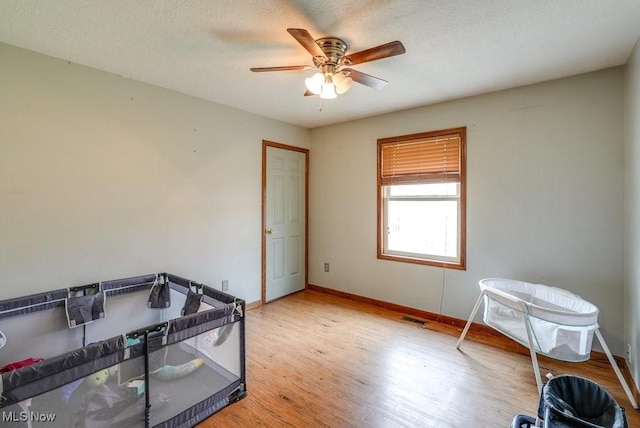 interior space featuring a textured ceiling, visible vents, baseboards, a ceiling fan, and light wood-type flooring