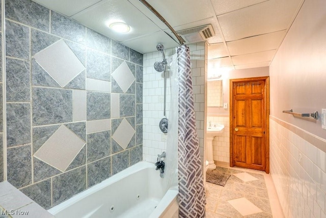 bathroom featuring tile walls, visible vents, a combined bath / shower with jetted tub, tile patterned flooring, and wainscoting