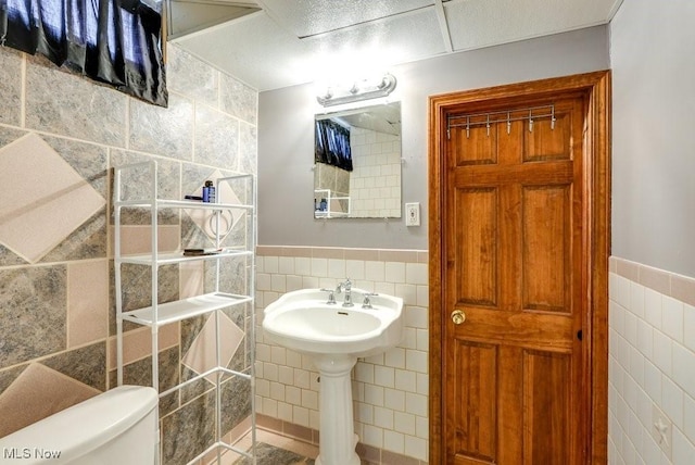 bathroom featuring a wainscoted wall, toilet, and tile walls