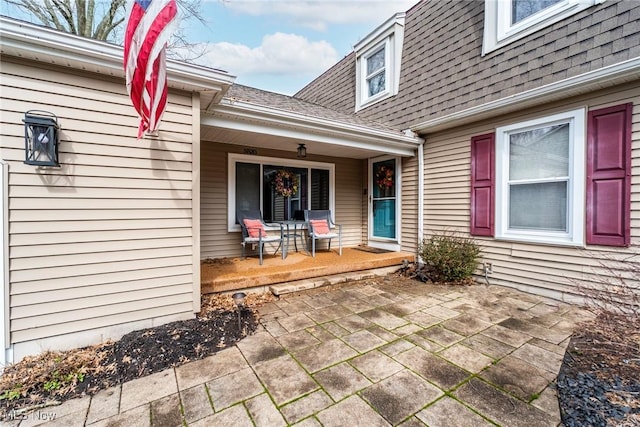 entrance to property with covered porch and a shingled roof
